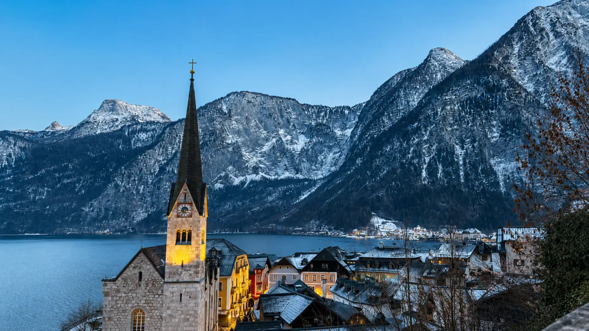 Church tower beside a lakeside village with snow-covered mountains in Austria.