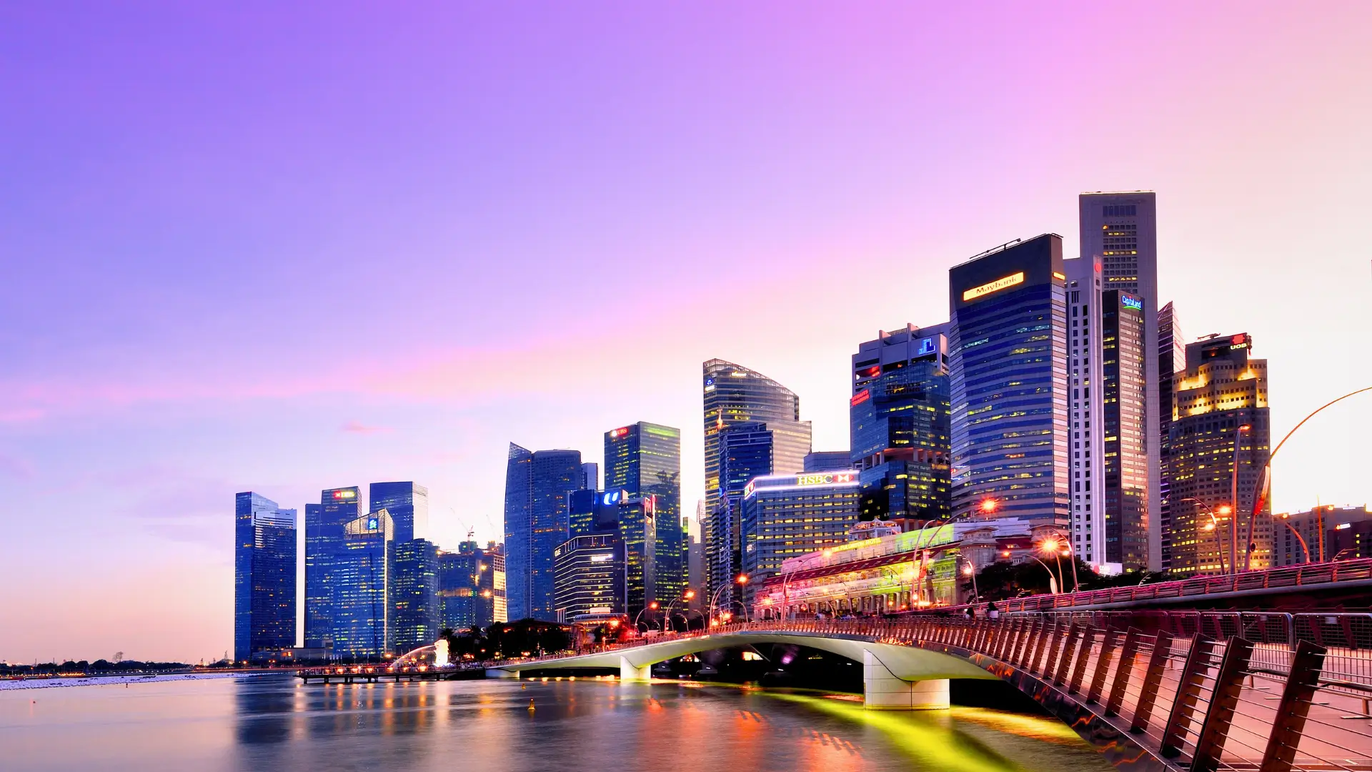 Singapore skyline at sunset with modern skyscrapers reflected on the waterfront.