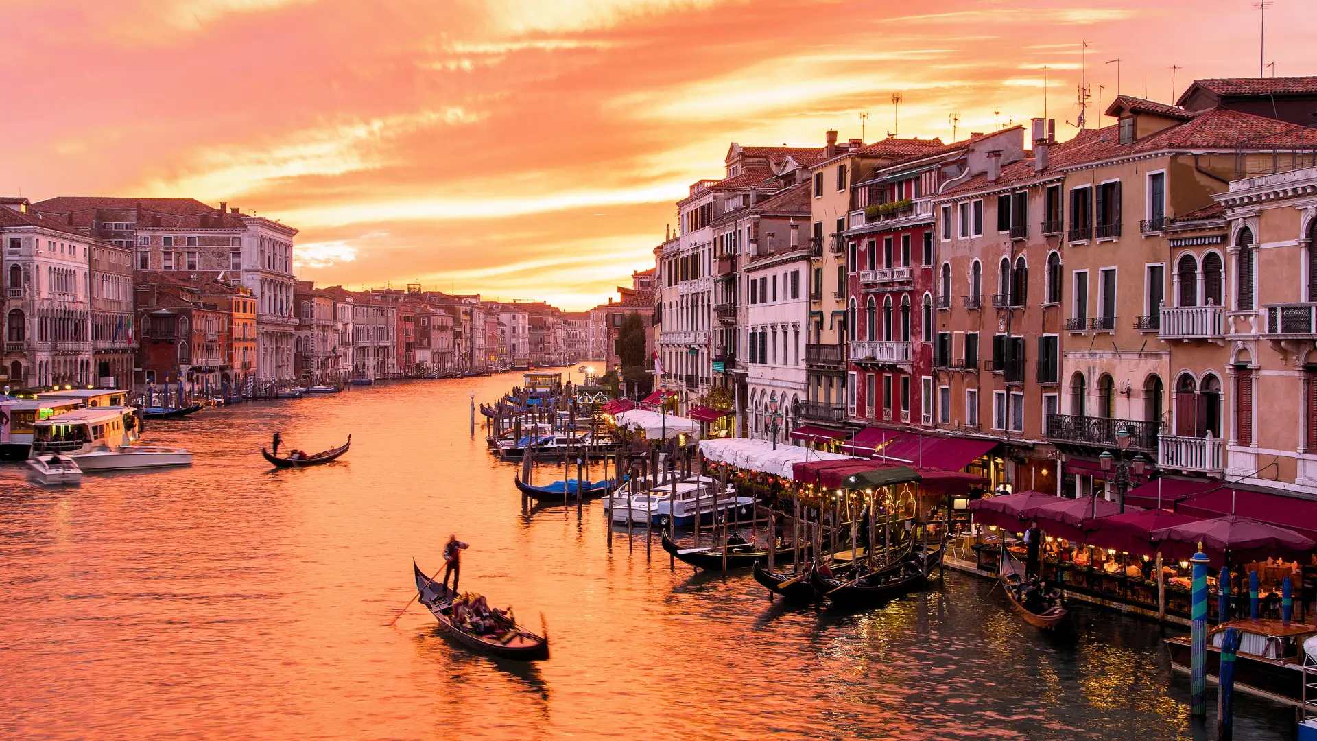 Sunset over the Grand Canal in Venice with gondolas and historic Italian buildings.