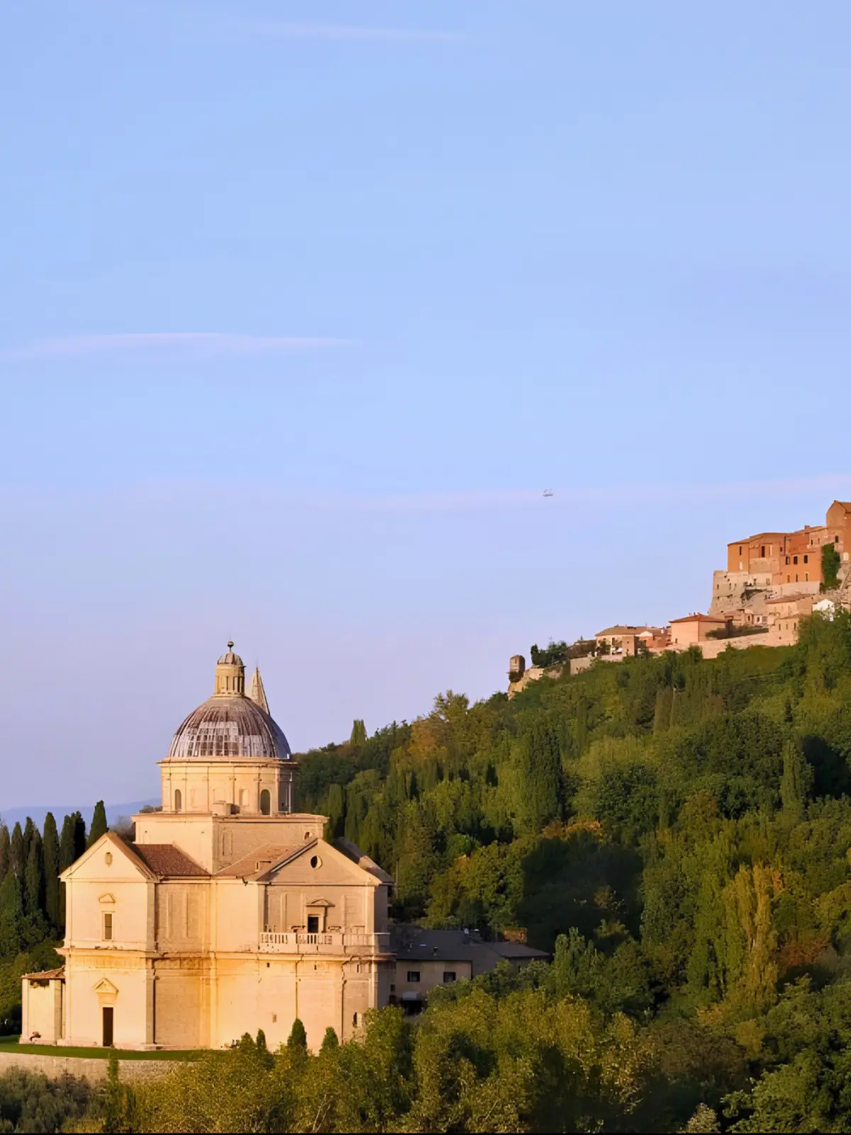 Hillside church surrounded by greenery under a soft blue sky.