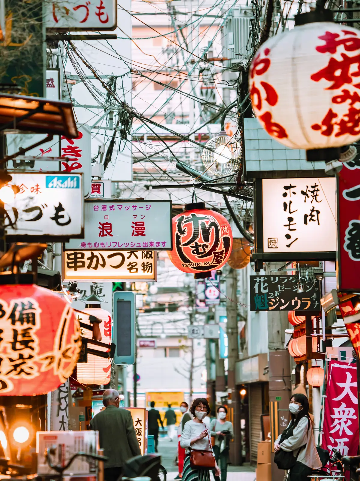 Lantern-lit street in Japan with traditional shop signs and pedestrians.
