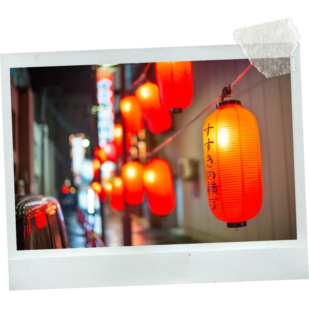 Red paper lanterns hanging along a narrow street at night in Japan.