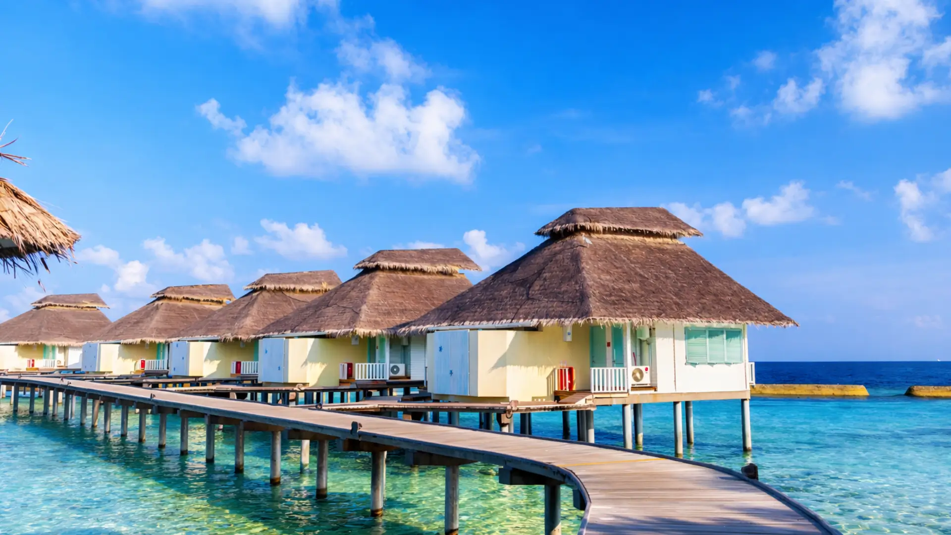 Overwater bungalows on wooden stilts connected by a curved boardwalk in Maldives.