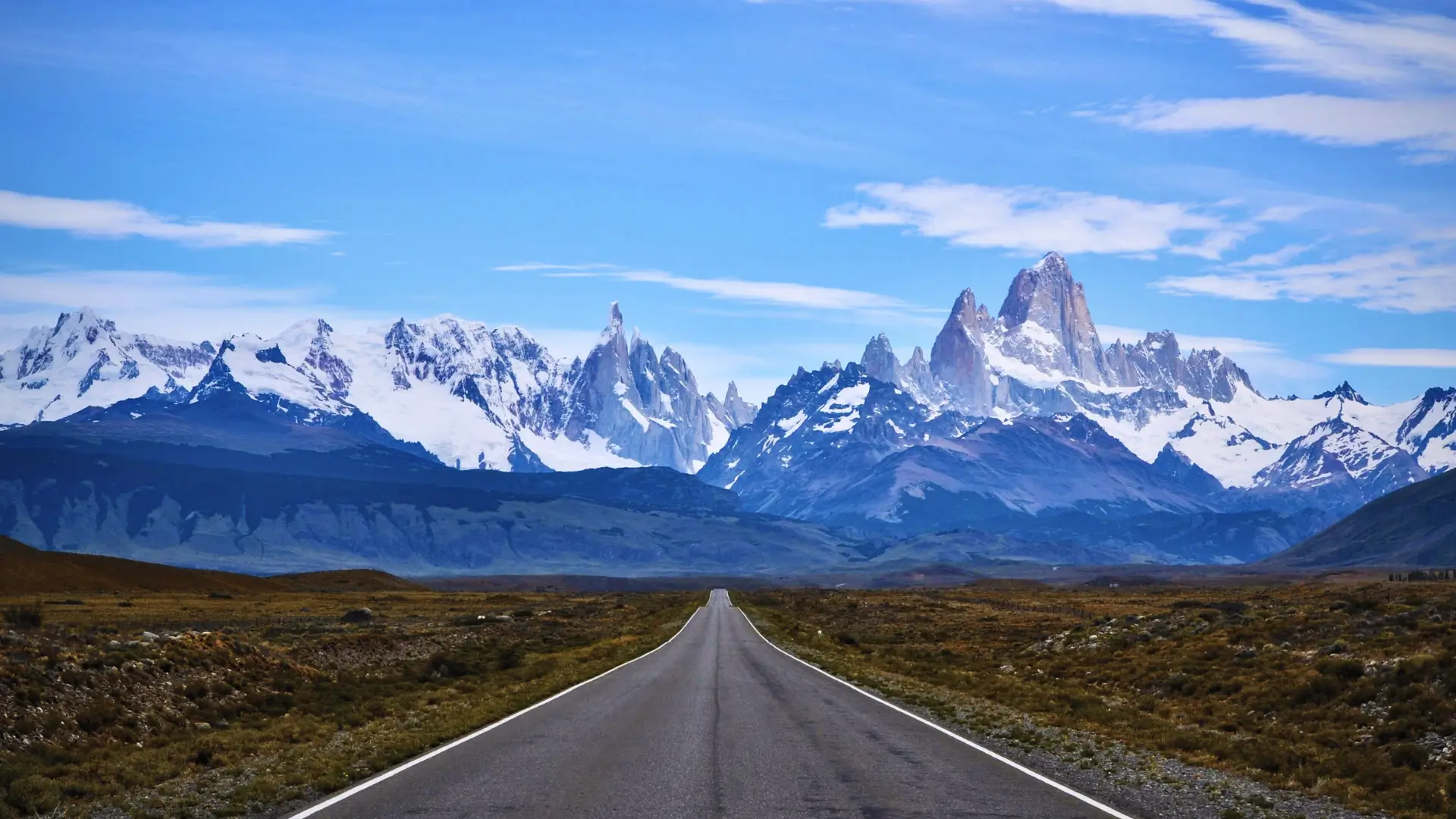 Open road in Patagonia framed by distant snow-covered Andes mountains.