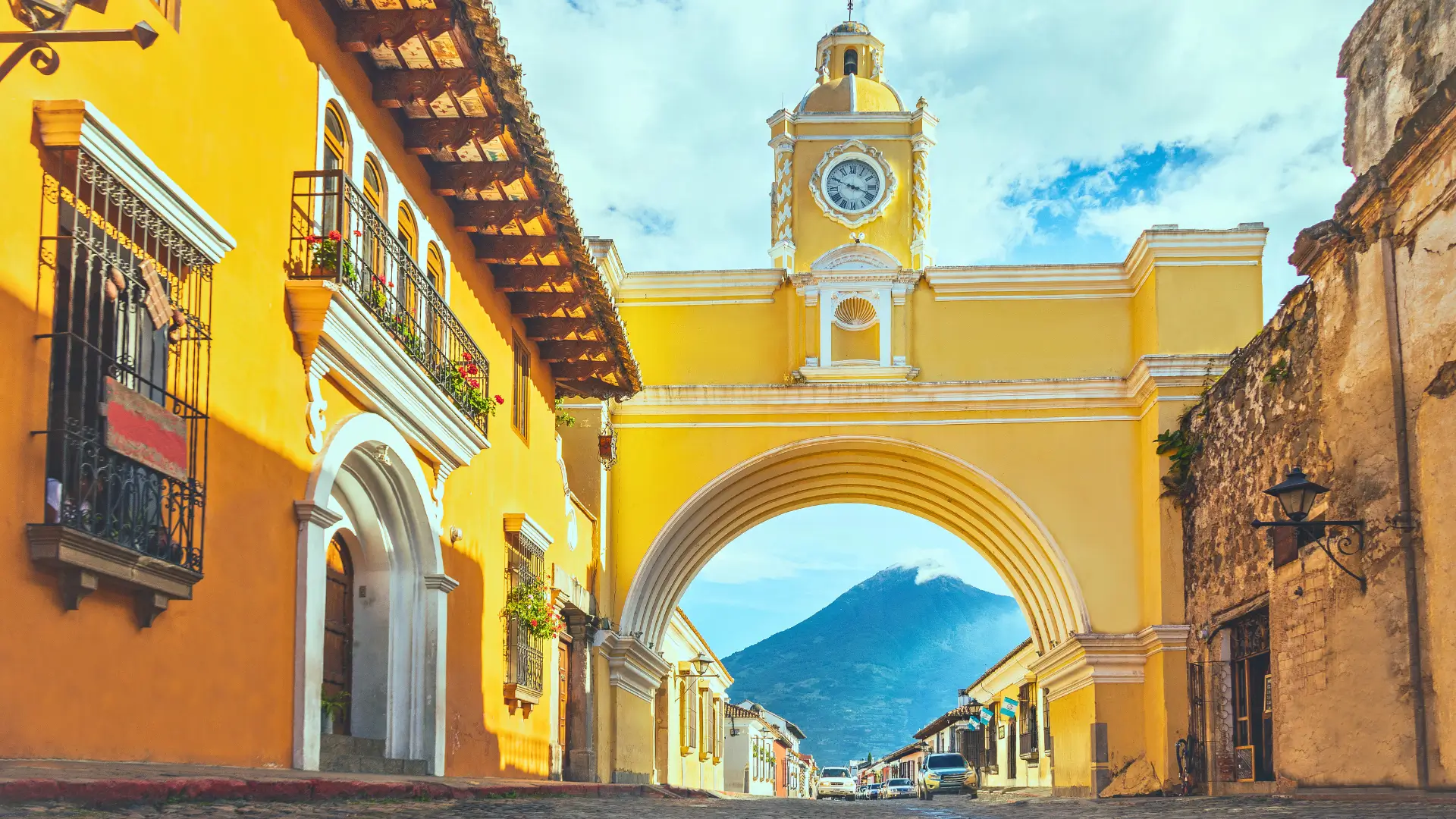 Yellow arch in Antigua with a volcano visible through the centre and colonial buildings lining the street.