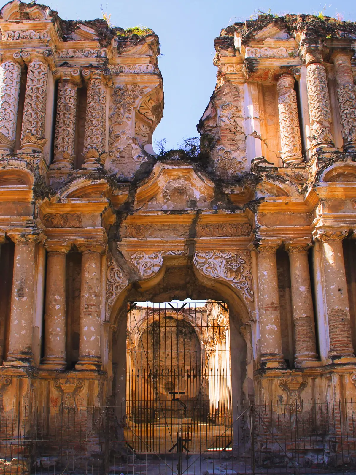 Colonial baroque church ruins in Antigua, Guatemala, with ornate stone façade and arched entrance.