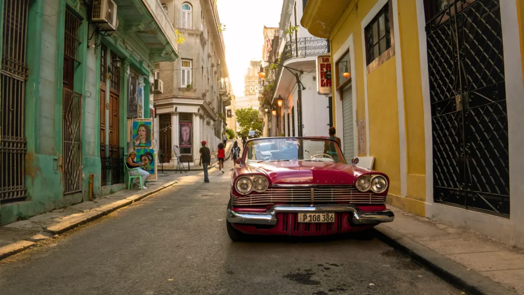 A classic vintage car parked on a narrow street in Havana, surrounded by colonial buildings and pedestrians.
