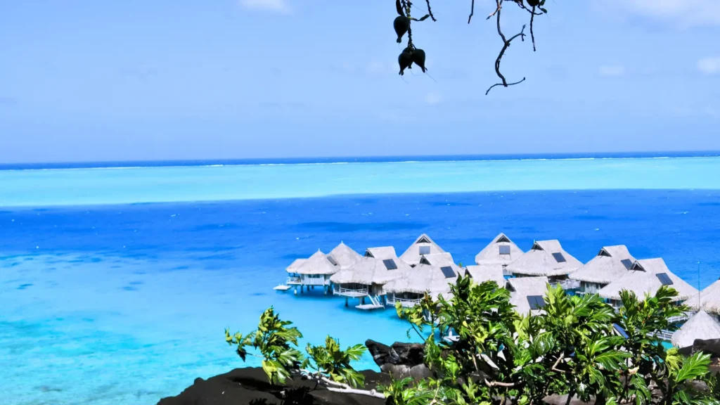 Overwater bungalows on turquoise lagoon with clear blue sky and tropical island setting.