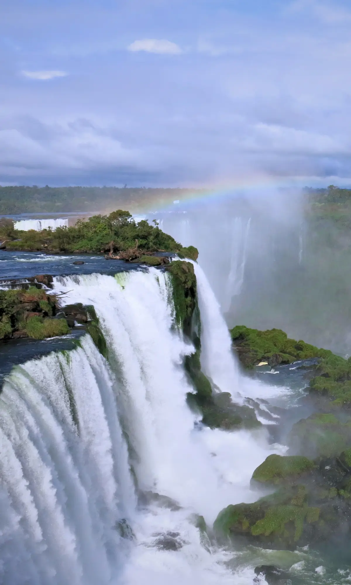 Iguazu Falls in Brazil with mist rising and a rainbow above the waterfall.