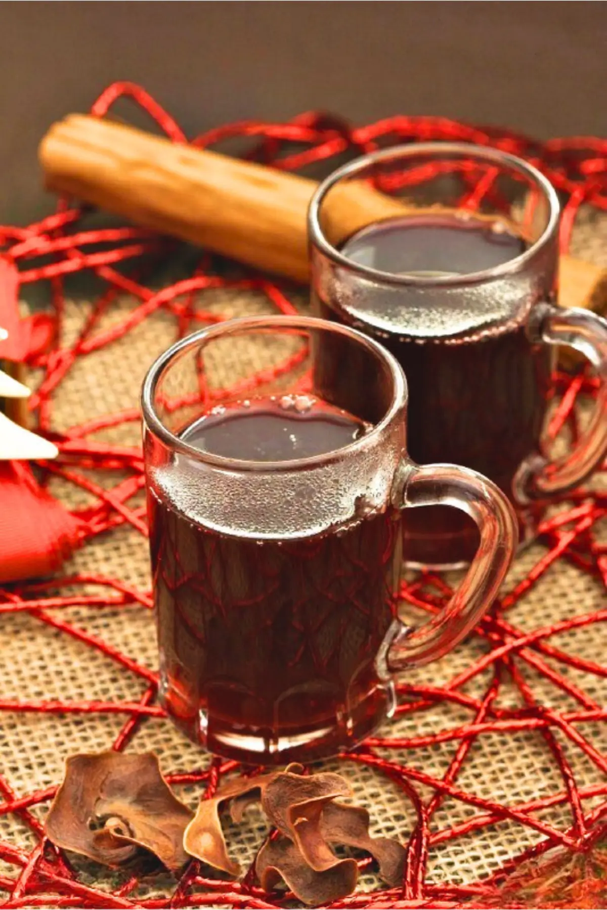 Two glass mugs of mulled wine with cinnamon stick and holiday decorations.