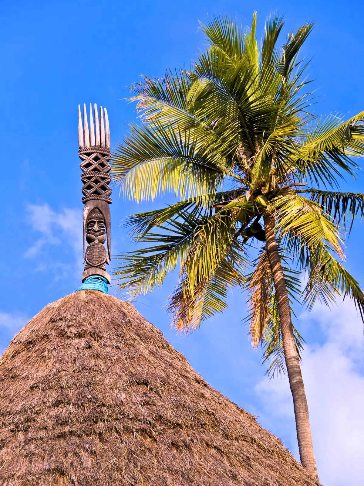 Traditional Kanak hut with carved totem and palm tree in New Caledonia.