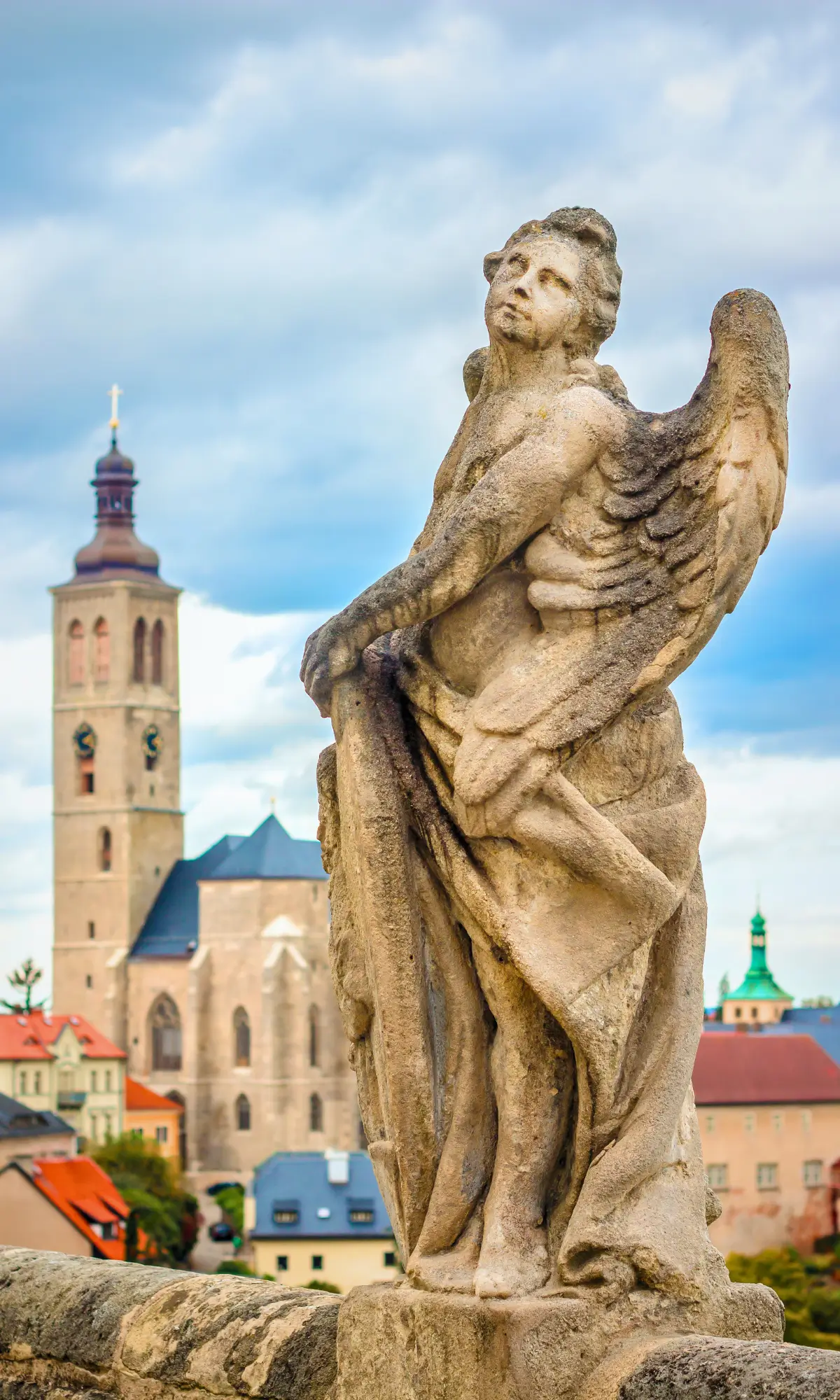 Baroque statue overlooking Kutná Hora with St. Barbara’s Cathedral and historic rooftops in the background.