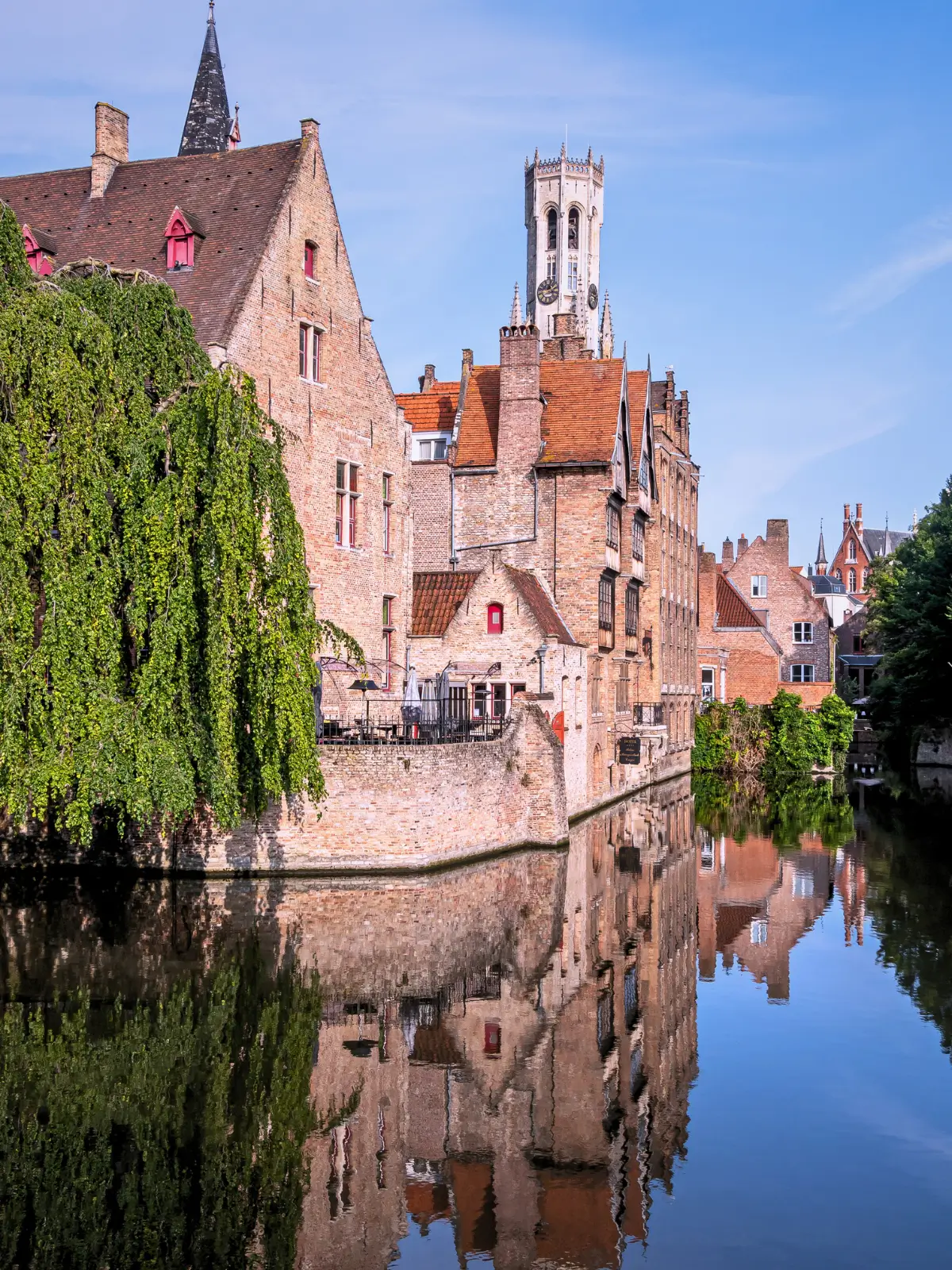 Medieval brick houses and church tower reflected in a calm canal in Bruges, Belgium.