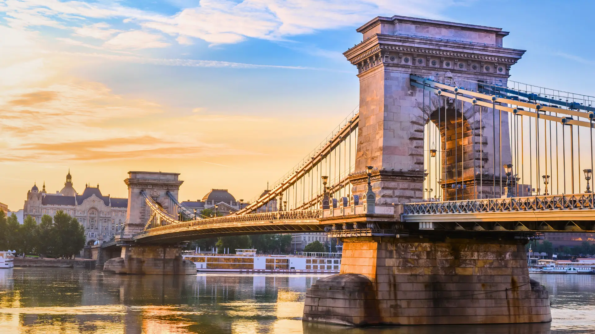 Side view of the Chain Bridge over the Danube River with historic buildings in Budapest.
