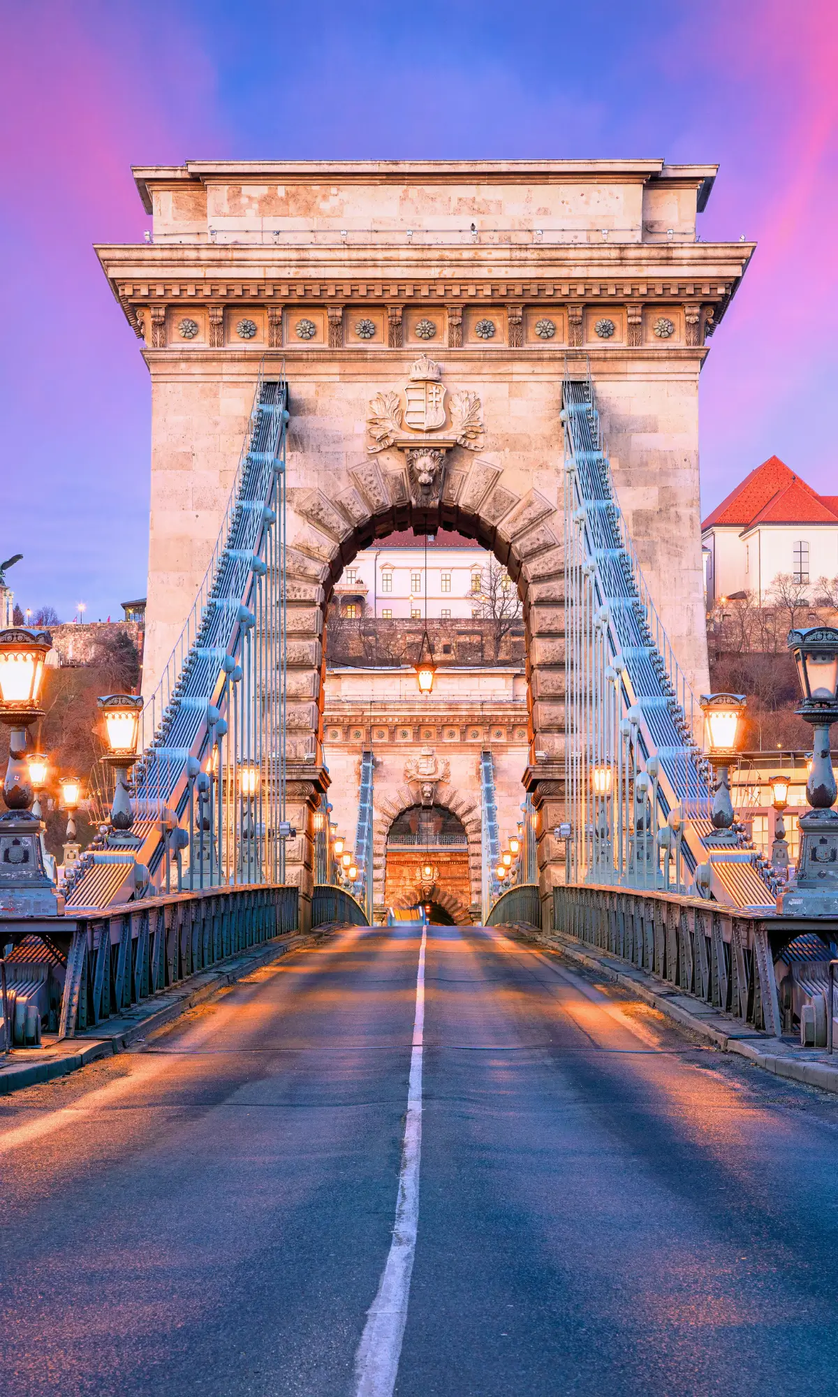 Front view of the Chain Bridge in Budapest with suspension cables and stone arch at dusk.