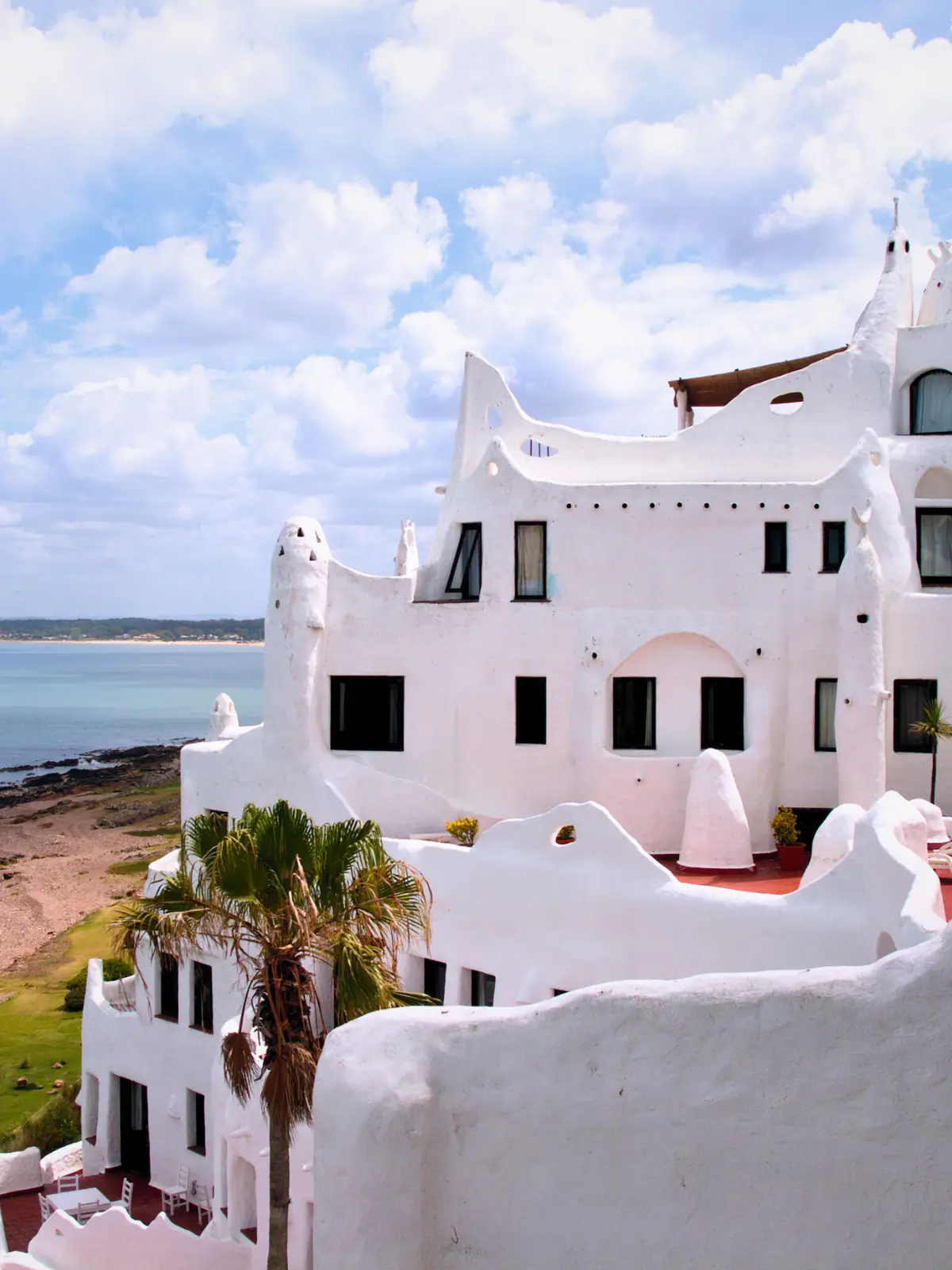 White stucco coastal building overlooking a quiet beach with soft clouds and calm sea in Uruguay.