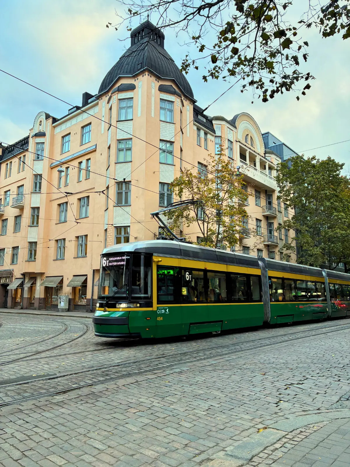 Green tram passing through a historic street in Helsinki.