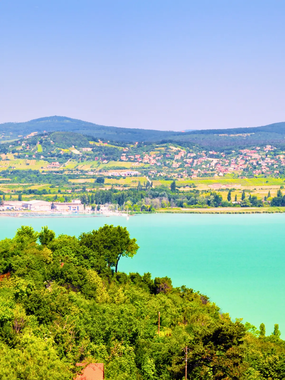 View over Lake Balaton with green hills, lakeside town, and calm turquoise water.