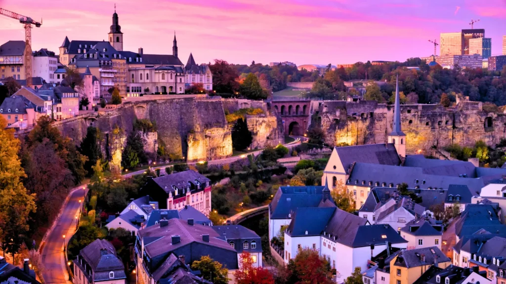 Cliffs and historic fortifications above old town buildings at sunset in Luxembourg.