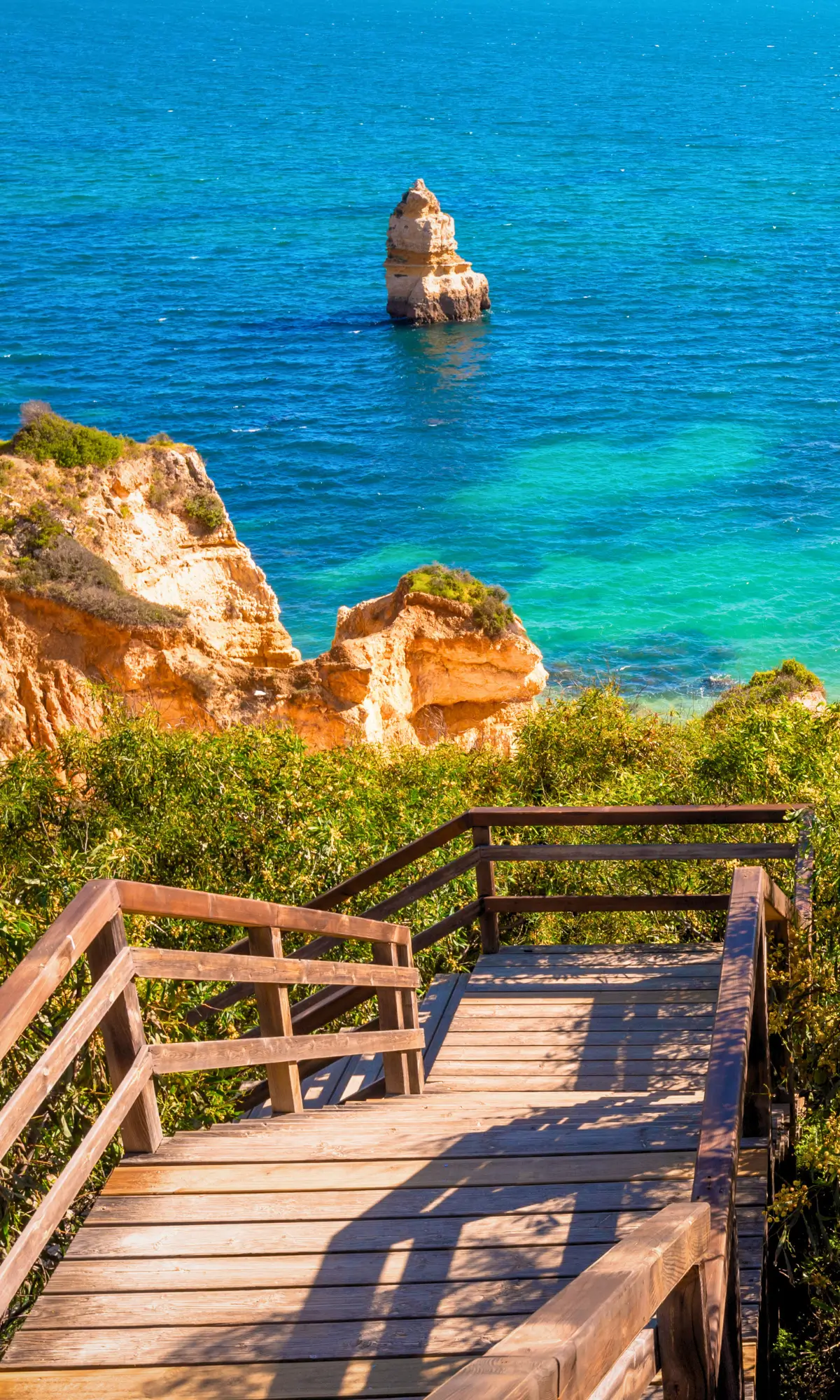 Wooden stairs leading down to golden cliffs and turquoise sea along the Algarve coast in Portugal.