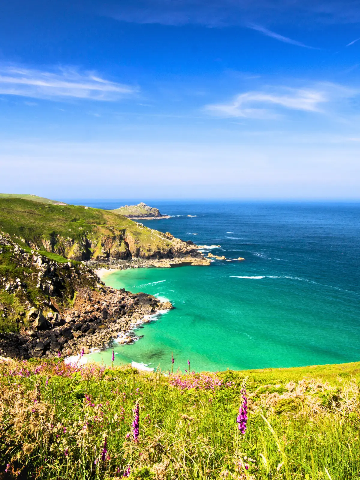 Coastal cliffs and turquoise water at a bay in Cornwall with clear skies and rugged shoreline.