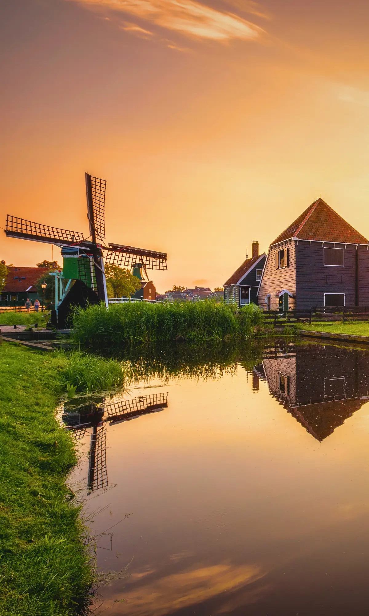 Windmill and traditional houses by a canal at sunset in the Netherlands.