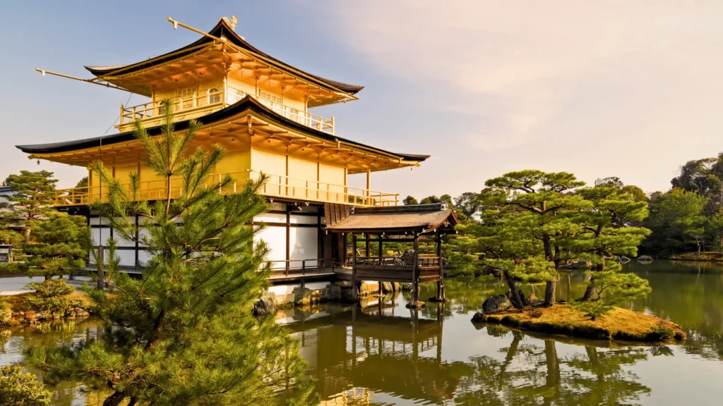 Kinkaku-ji Golden Pavilion beside a calm pond with pine trees.