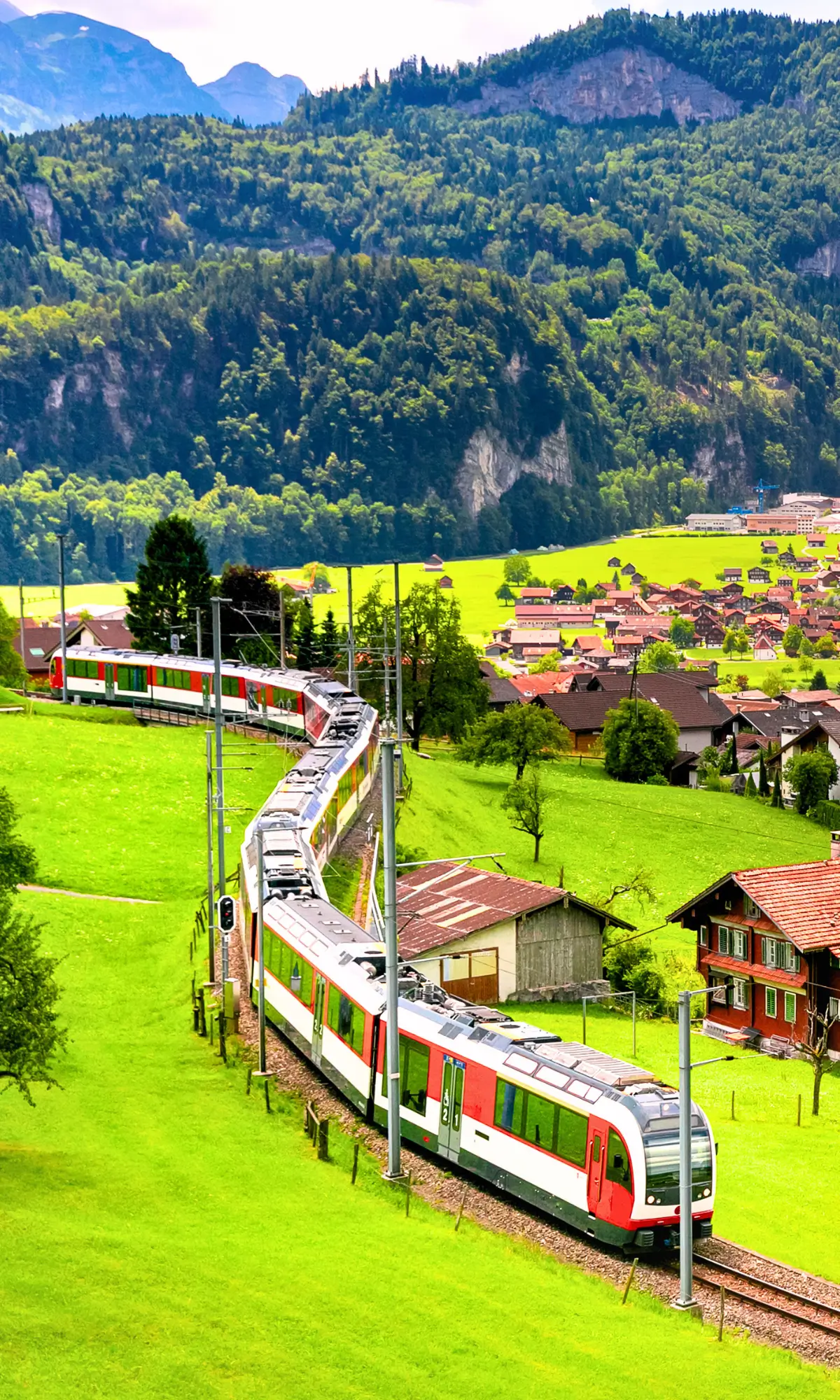 Train passing through Lauterbrunnen Valley with green fields and mountain cliffs around.