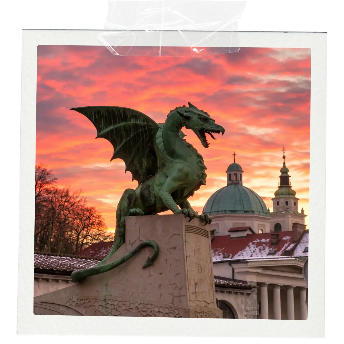 Dragon statue on Dragon Bridge in Ljubljana at sunset with historic buildings behind.