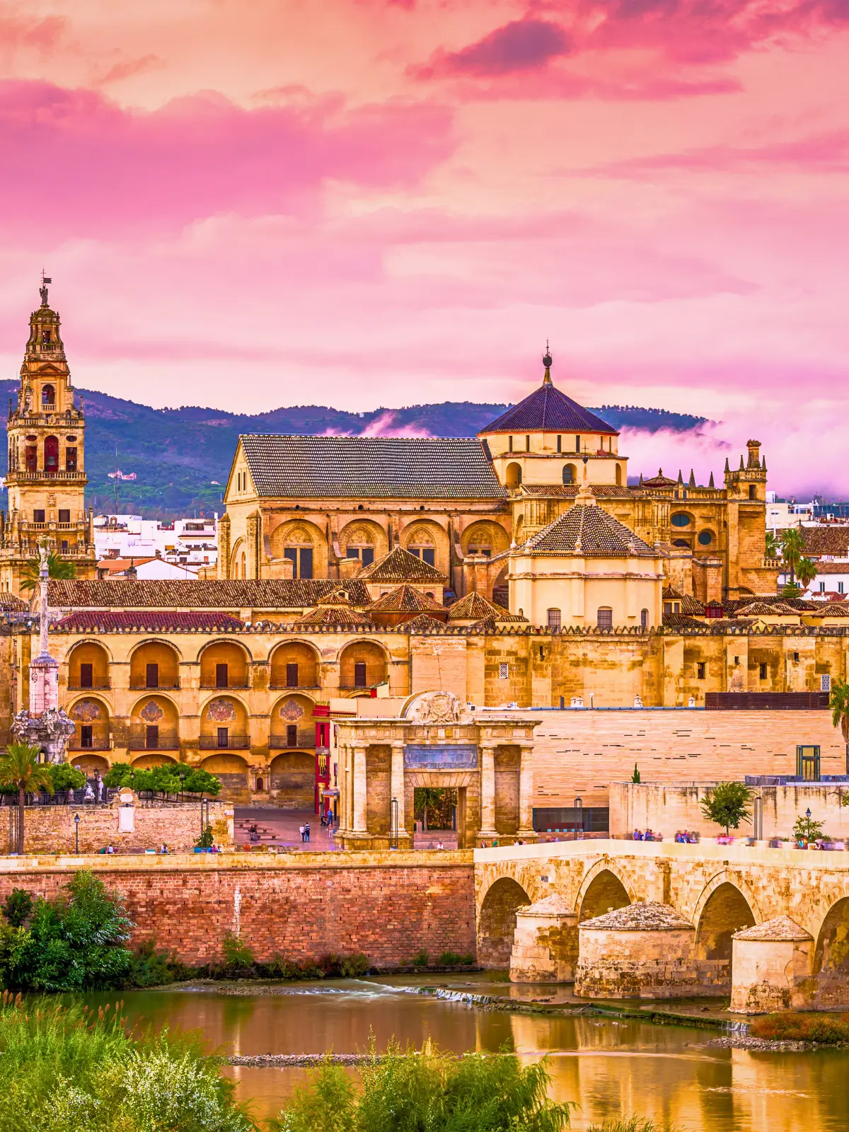 Mezquita-Catedral de Córdoba with Roman bridge and river at sunset.