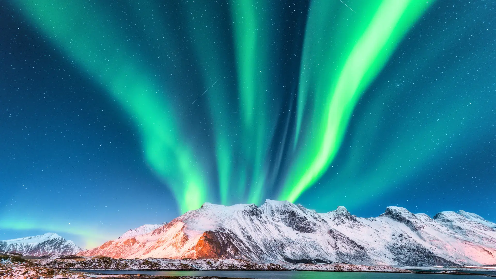 Northern lights over snowy mountains in Norway under a clear night sky.