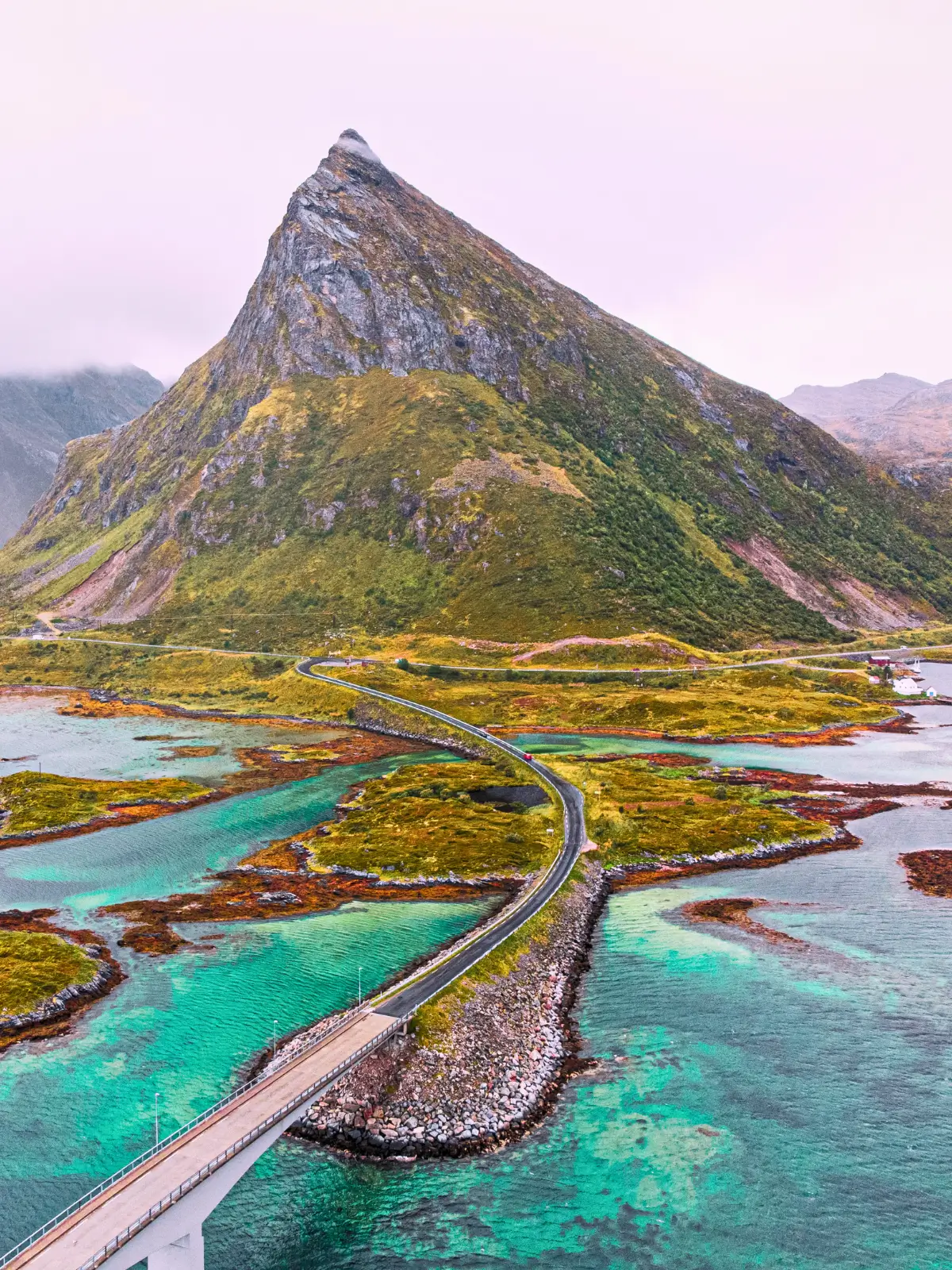 Scenic coastal road crossing turquoise waters with mountains in the Lofoten Islands, Norway.