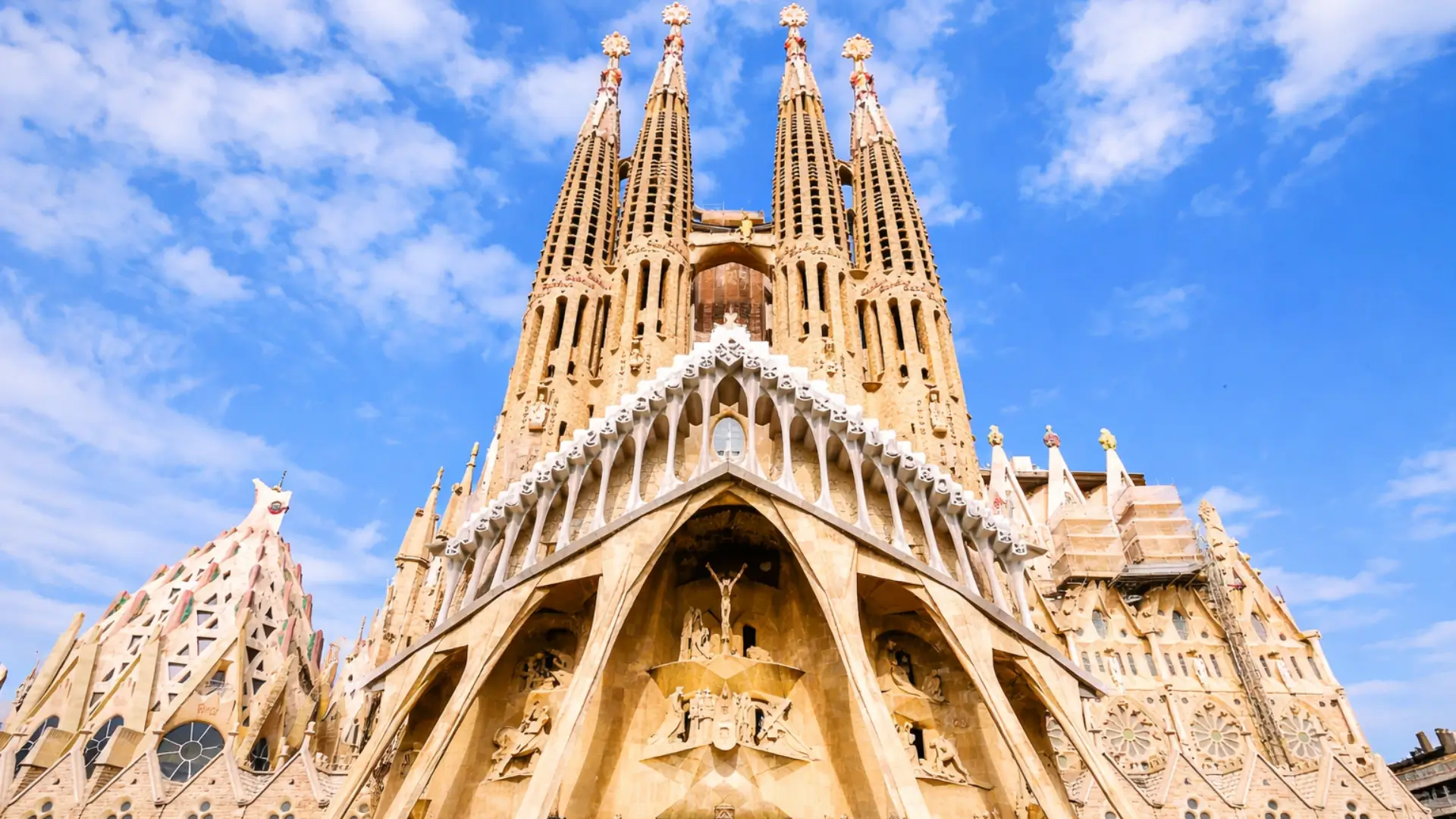 Sagrada Familia in Barcelona with towering spires and intricate facade details against a bright blue sky.