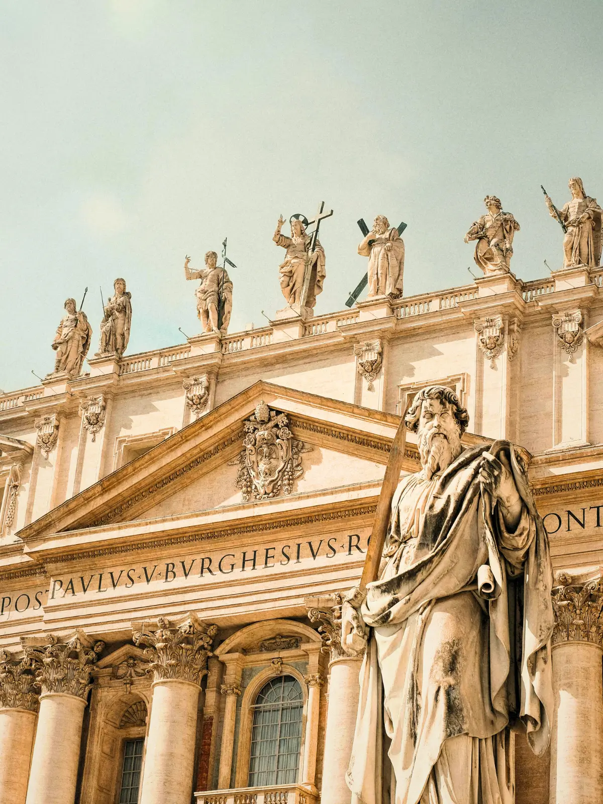 Statue of Saint Peter in front of St Peter’s Basilica facade with rooftop statues in Vatican City.