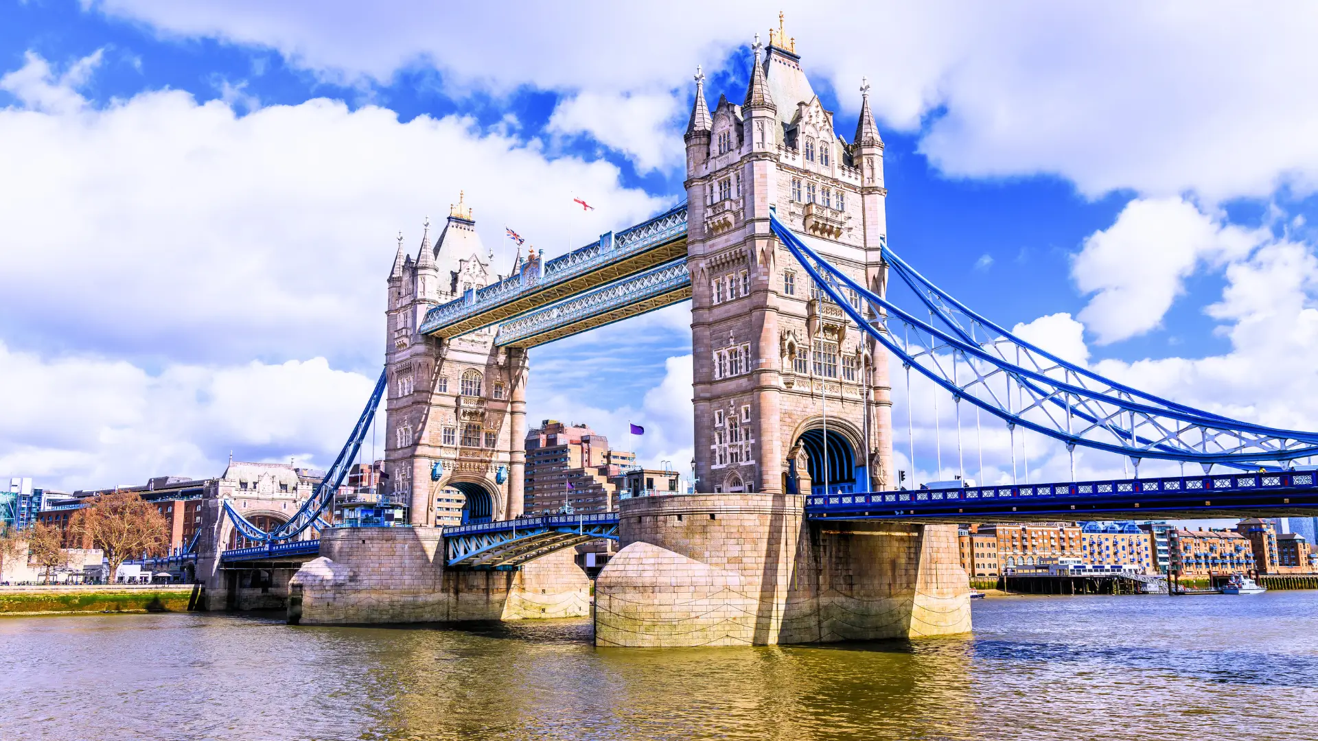 Tower Bridge in London spanning the River Thames with blue suspension elements and city backdrop.
