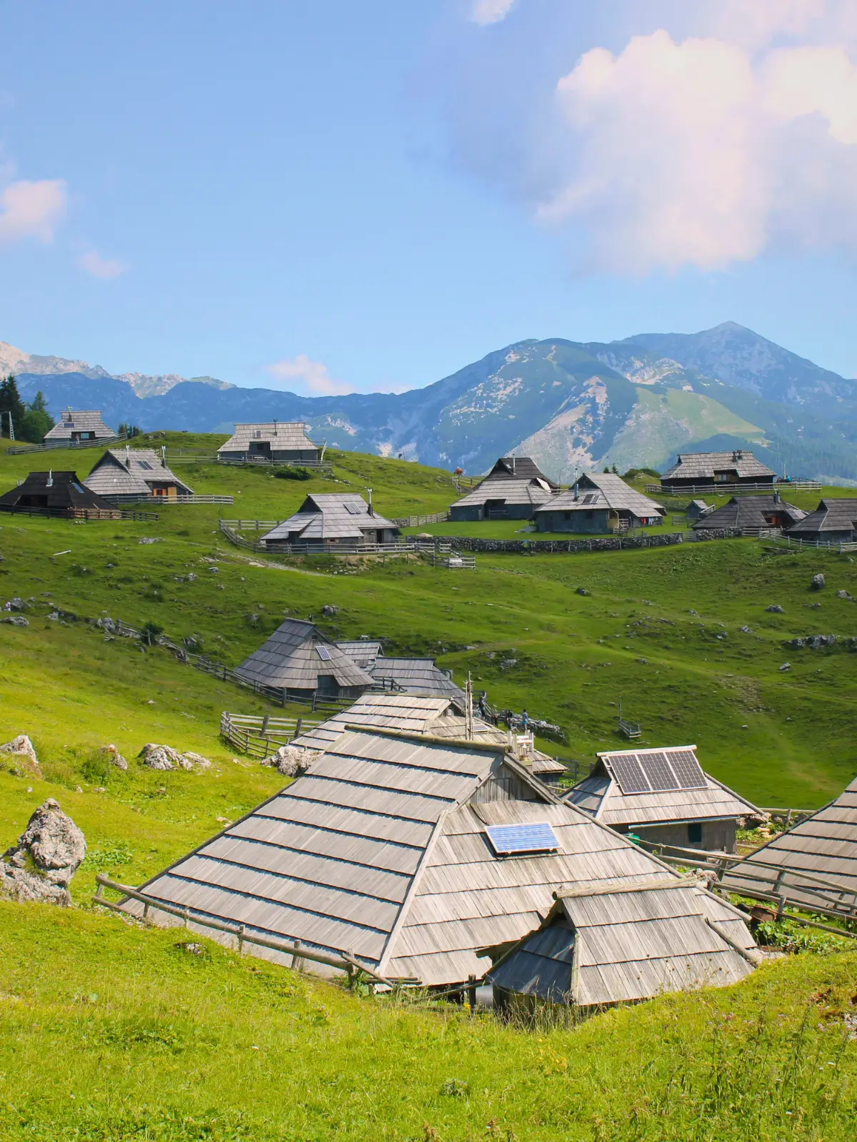 Wooden huts scattered across green hills in Velika Planina with mountains in the background.