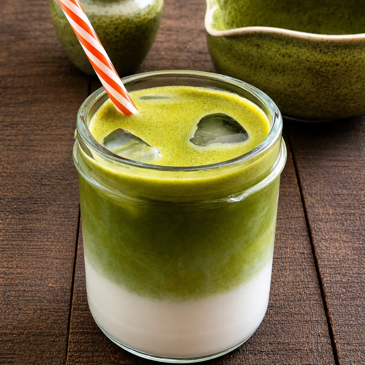 Iced matcha latte in a glass jar with layered milk and matcha served on a rustic wooden table.