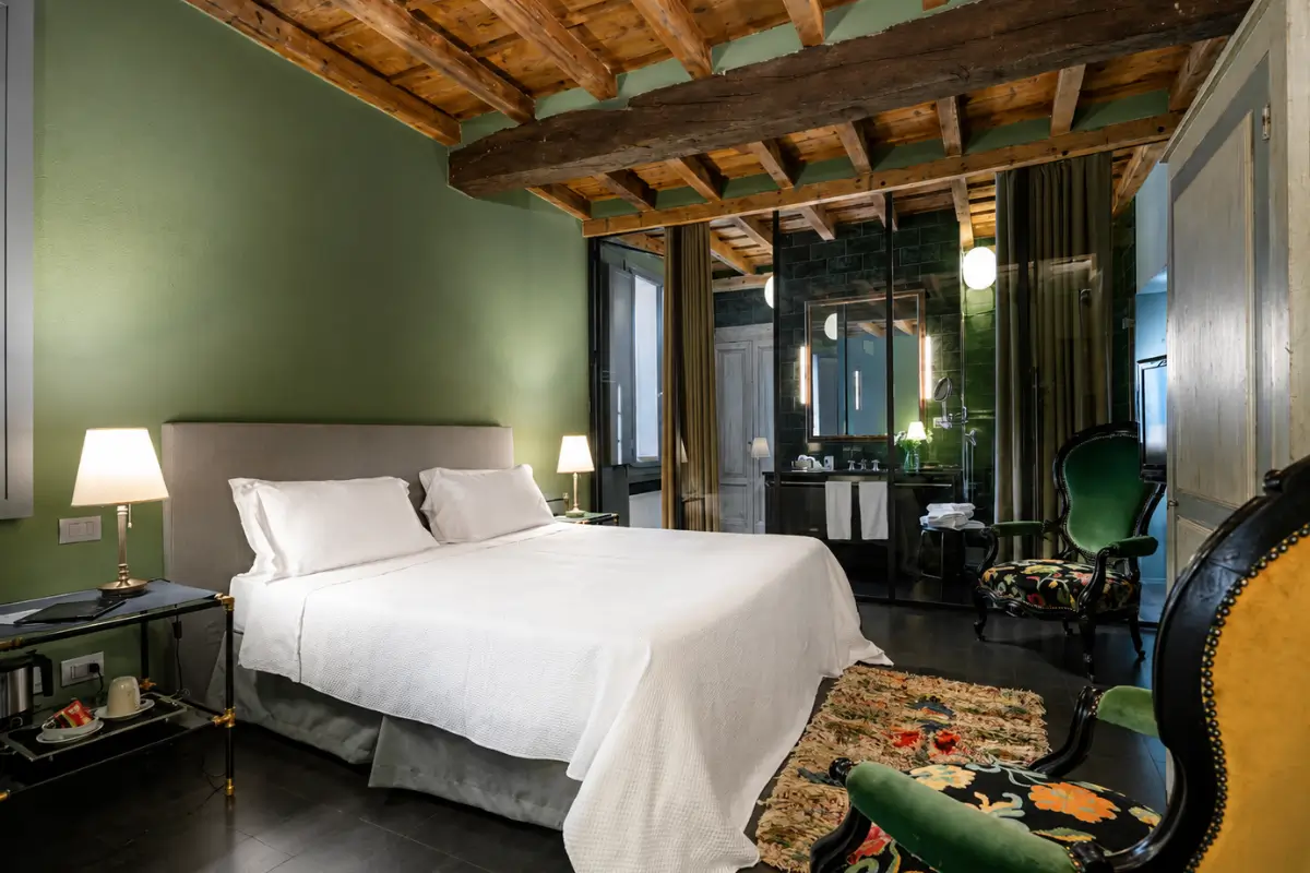 Maison Borella hotel room with green walls, wooden ceiling beams, and a white bed.