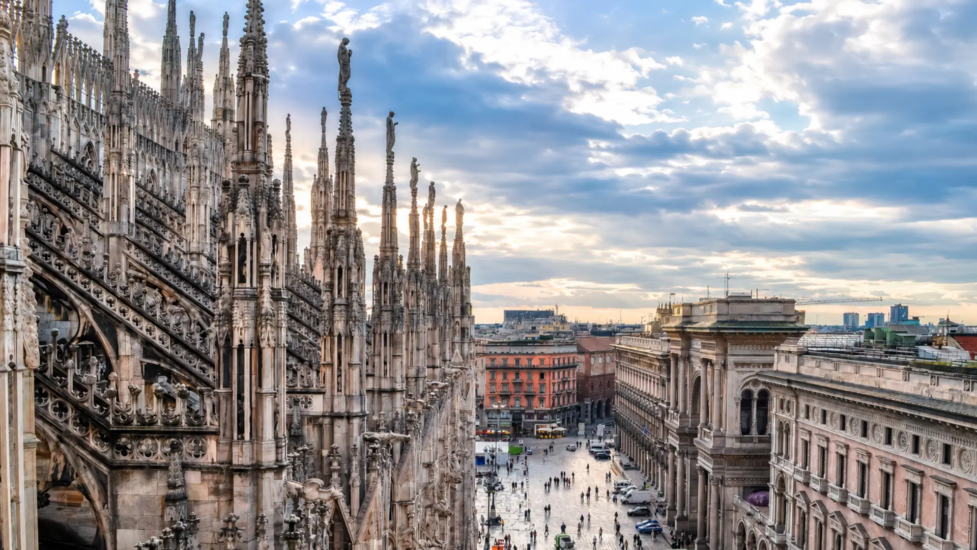 View across the Duomo rooftop and central Milan buildings at sunset.