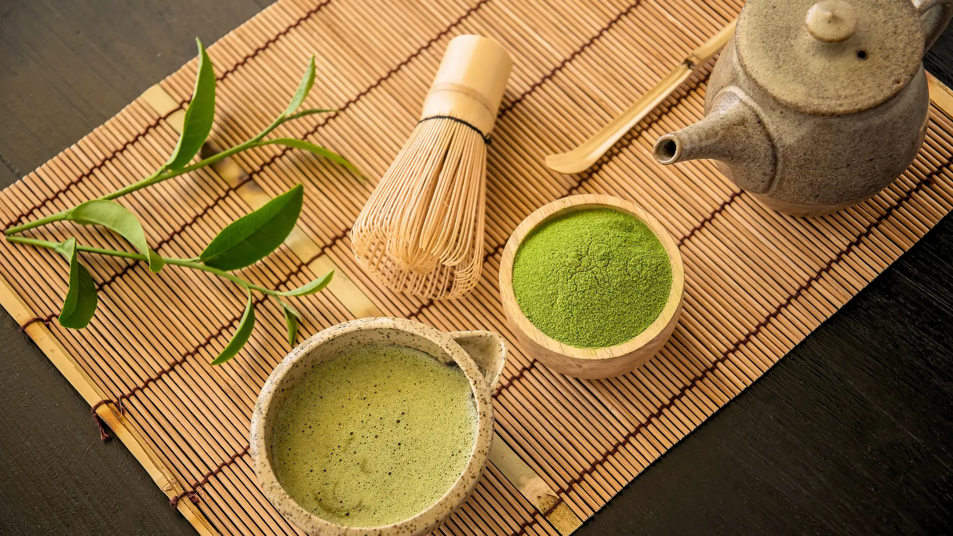 Traditional tea ceremony Kyoto set with matcha tea, bamboo whisk, ceramic teapot, and fresh green tea leaves.