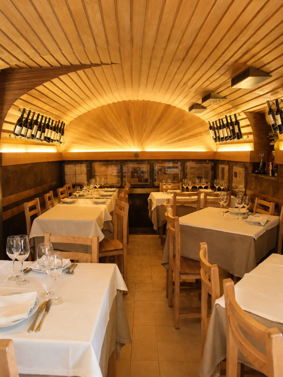 Dining room at Adega São Nicolau in Porto with wooden tables and wine bottles on display.