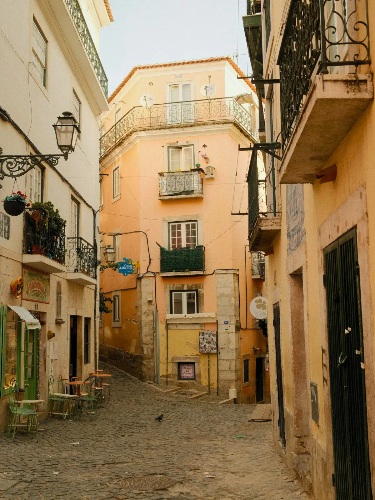A narrow cobblestone street lined with colourful historic buildings and wrought-iron balconies in Alfama, Lisbon.