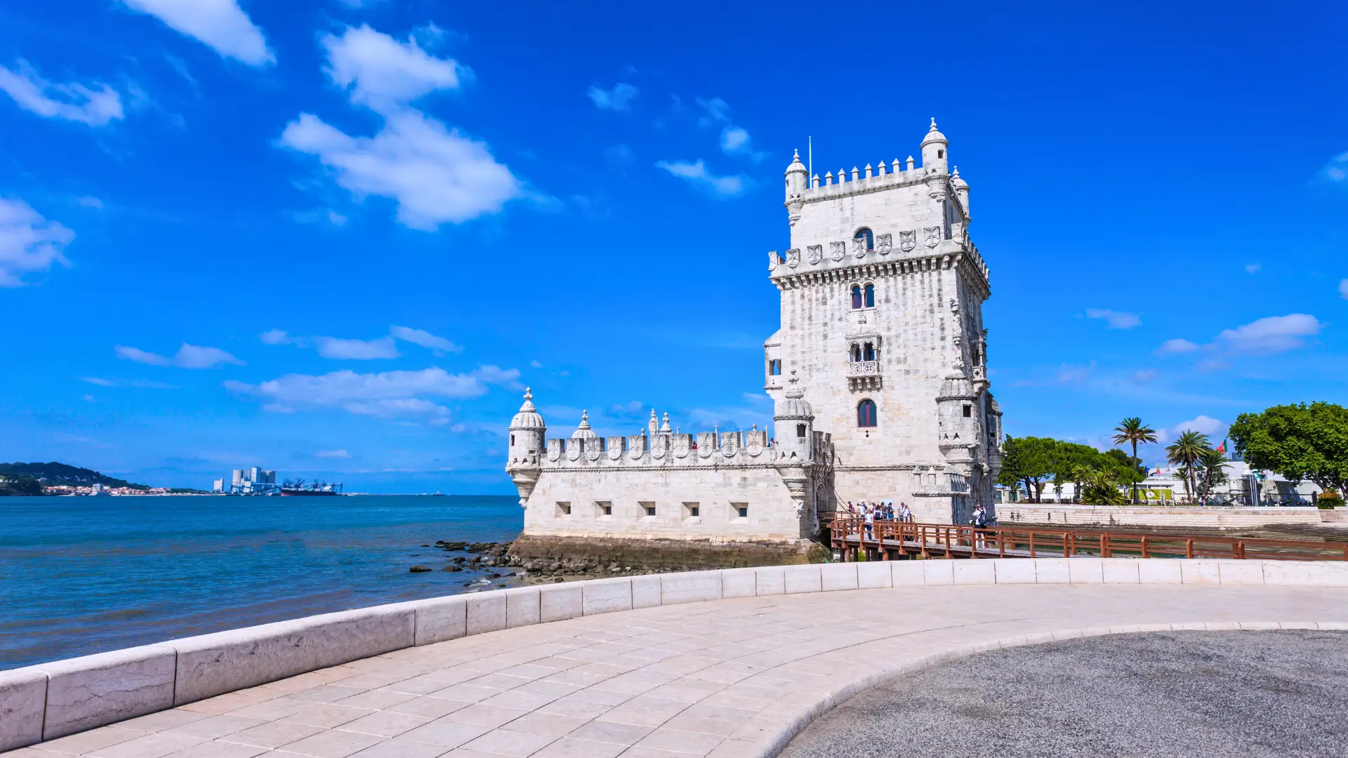 The historic stone Belem Tower on the waterfront in Lisbon under a bright blue sky.