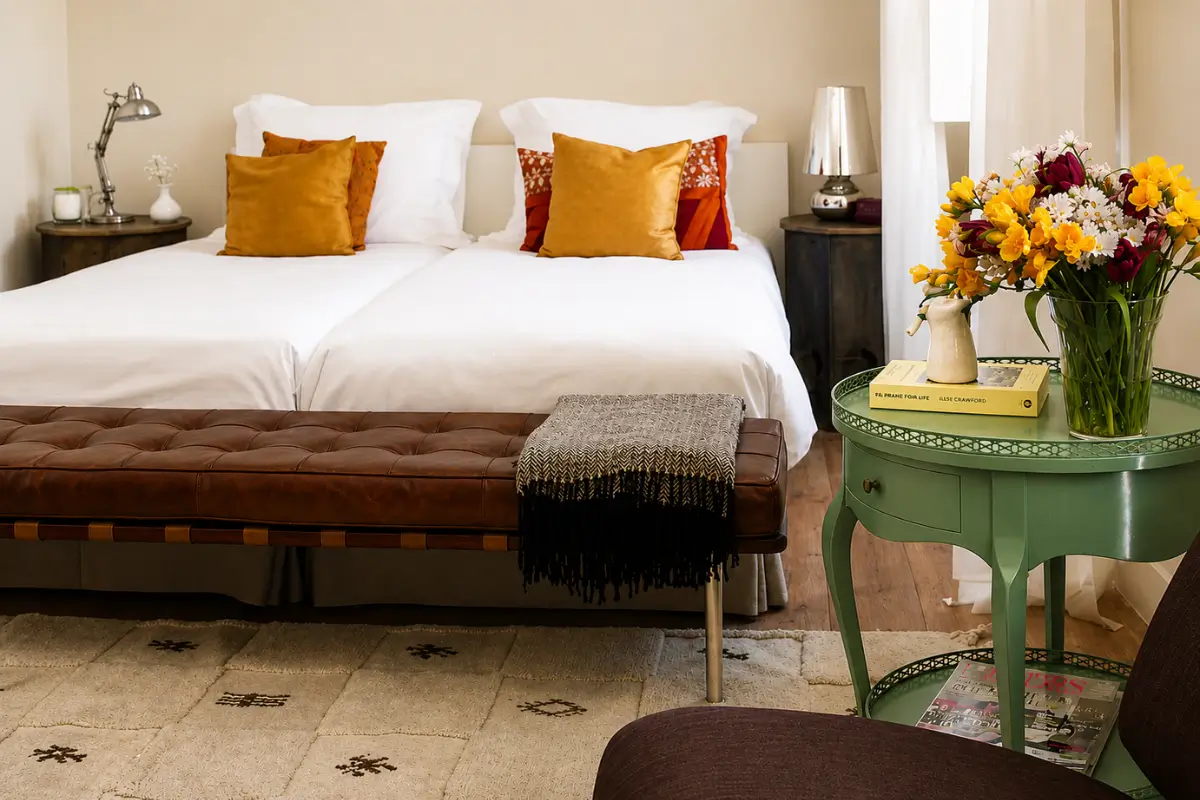 Bright room at Casa das Janelas com Vista with twin beds, a leather bench and colorful flowers.