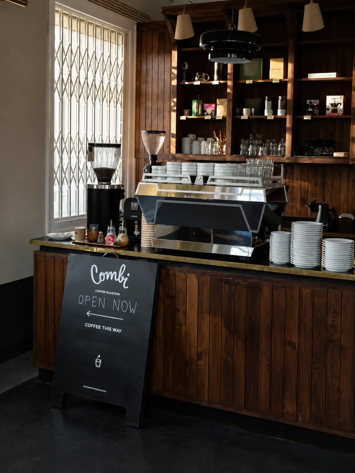Coffee bar inside Combi Coffee Roasters in Porto with an espresso machine and wooden shelving.