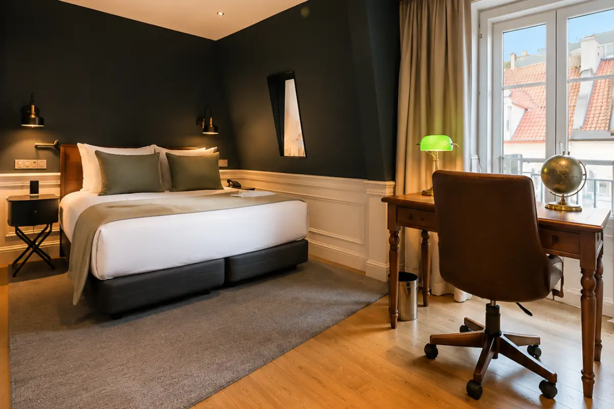 Boutique hotel bedroom with a double bed, dark green walls, wooden writing desk, and balcony.