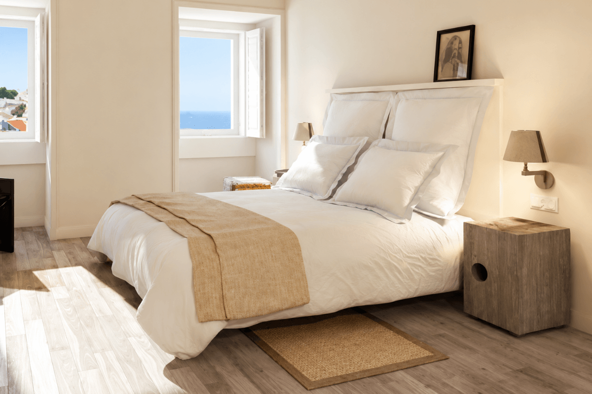 Bright Lisbon hotel room with white bedding and sea views from the windows.