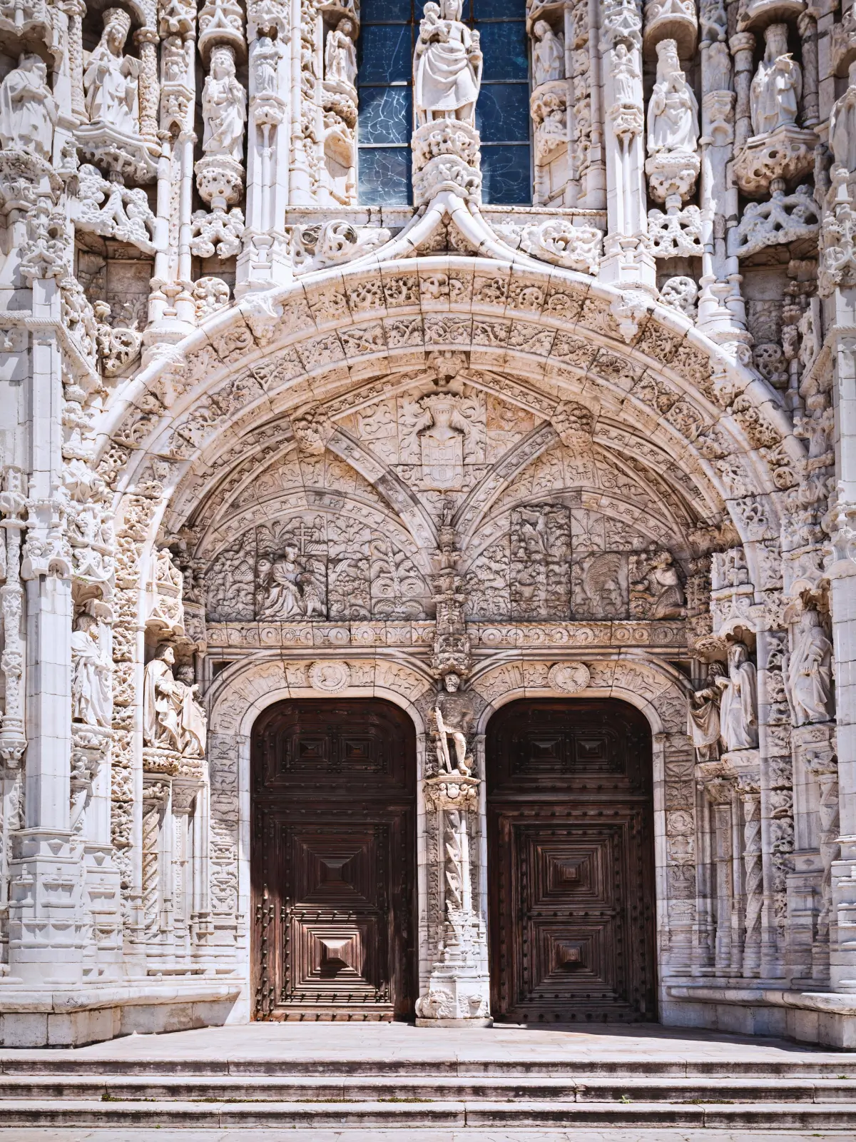 Intricate carved limestone arches and statues surrounding the wooden entrance doors of Jerónimos Monastery in Lisbon.