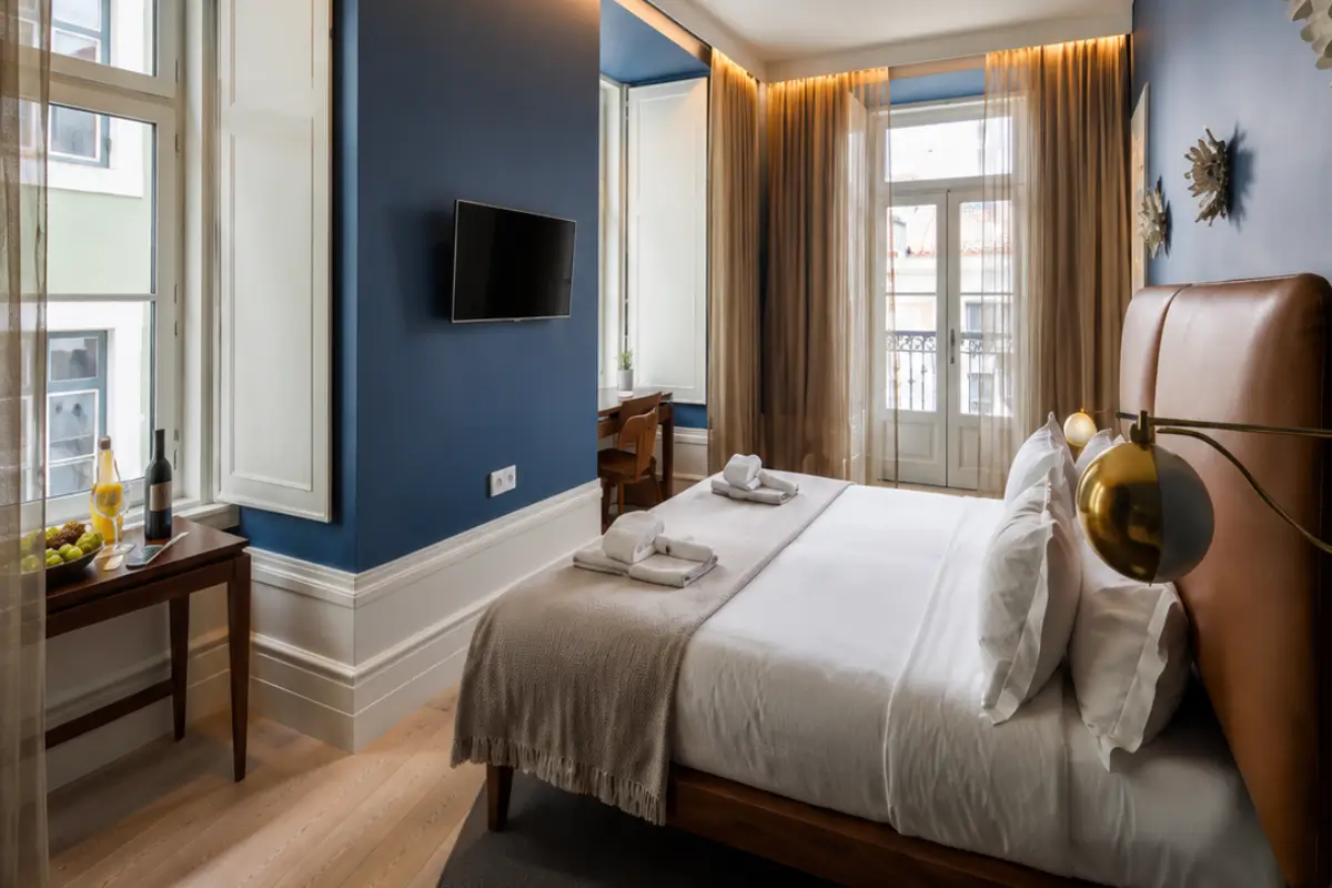 Modern hotel bedroom with deep blue walls, a leather headboard bed, and balcony doors.