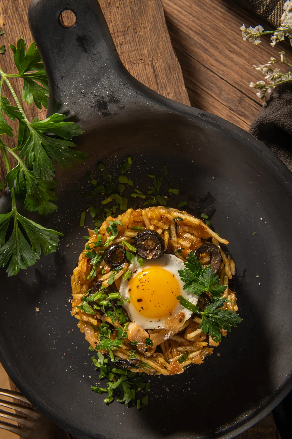 Portuguese dish with egg, potatoes, herbs and olives served in a dark pan.